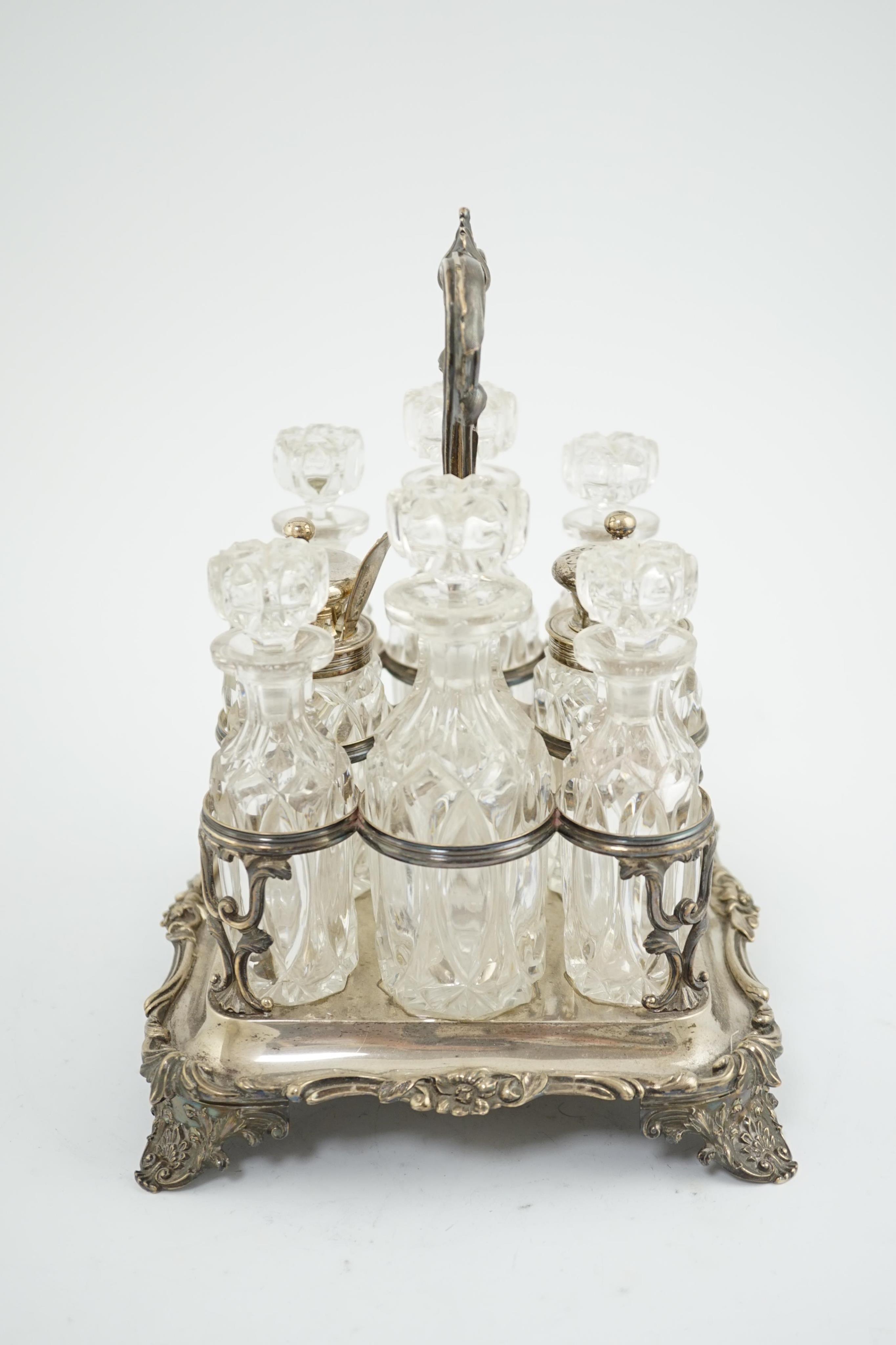 An early Victorian silver rectangular cruet stand, maker WE?, with single handle, foliate decoration and eight matching glass bottles, two with silver mounts and an associated spoon, London, 1837, stand height 26.8cm, 32